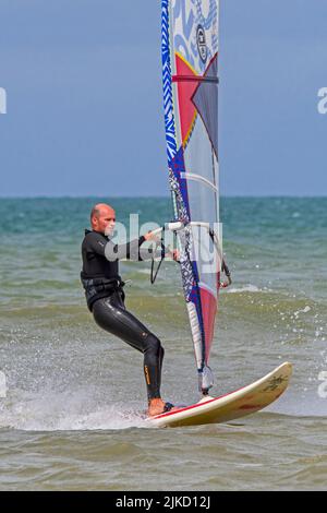 Planche à voile sportive en combinaison noire pratiquant la planche à voile classique le long de la côte de la mer du Nord Banque D'Images