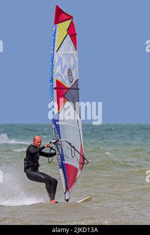 Planche à voile sportive en combinaison noire pratiquant la planche à voile classique le long de la côte de la mer du Nord Banque D'Images