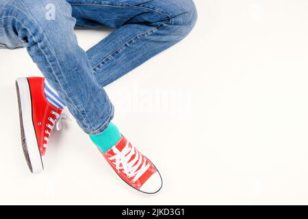 Enfant portant différentes paires de chaussettes. Pieds d'enfant dans des chaussettes et des baskets rouges mal assorties sur fond blanc. Journée des chaussettes impaires, semaine anti-intimidation Banque D'Images