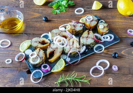 Maquereau fumé sur planche à découper, rondelles d'oignon, citron, olives, huile, vert sur fond en bois Banque D'Images