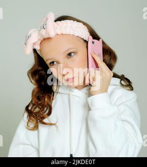 adolescente dans un sweat à capuche blanc dans le studio sur un fond blanc divers grimaces, elle est jeune elle a un téléphone mobile dans ses mains, elle prend un selfie et s'admire elle-même et un bandage rose. Banque D'Images