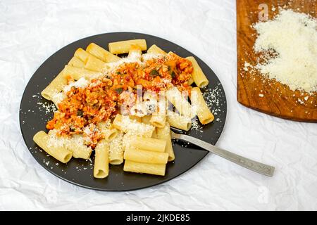 Pâtes bolognaises à la sauce ragu et au parmesan râpé, sur une assiette en céramique noire. Banque D'Images