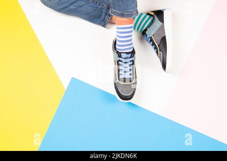 Enfant portant différentes paires de chaussettes. Pieds d'enfant en chaussettes mal assorties et baskets colorées sur fond blanc. Vue de dessus. Chaussettes impaires de jour, anti Banque D'Images