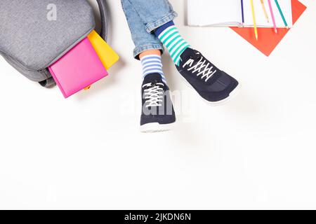 Enfant portant différentes paires de chaussettes. Bas enfant en chaussettes et baskets colorées, sac à dos avec livres et fournitures scolaires sur blanc Banque D'Images