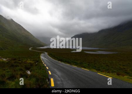 l'autoroute étroite à sommet noir avec des marquages de route jaunes mène à travers une vallée de montagne couverte de brouillard et de brume et des lacs à la base de la vallée Banque D'Images