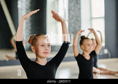 Jeune fille blonde en léopard noir gardant les bras levés au-dessus de la tête tout en pratiquant l'exercice chorégraphique à la leçon de danse Banque D'Images