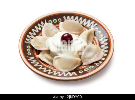 Boulettes ukrainiennes traditionnelles, varéniki aux cerises et à la crème aigre dans un bol en céramique peint isolé sur fond blanc. Banque D'Images