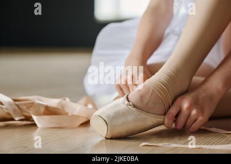 Gros plan des mains d'un danseur de ballet mettant sur la chaussure pointe avant la répétition tout en étant assis sur le plancher de la salle de classe ou du studio Banque D'Images