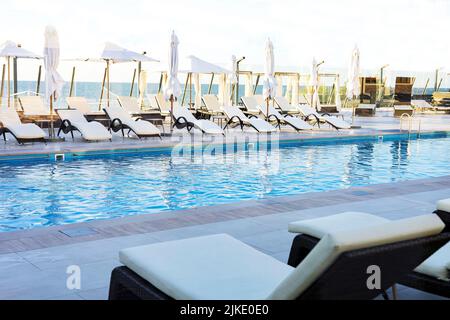 Parasol et chaise longue autour de la piscine extérieure dans le complexe de l'hôtel près de la mer plage océan pour les vacances de voyage Banque D'Images