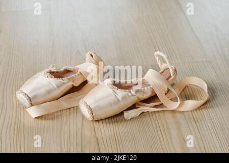 Paire de nouvelles chaussures de pointe déliées de couleur beige avec rubans de soie sur le plancher de la salle de danse ou de la salle de classe pour des répétitions d'exercices de ballet Banque D'Images