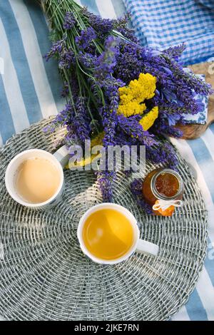 bouquet d'été d'yarrow jaune et de lavande violette, 2 tasses de thé au lait et un pot de confiture de mandarine sur une couverture de pique-nique rayée avec une atmosphère d'été Banque D'Images