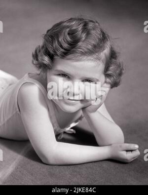 1930S MIGNONNE PETITE FILLE COUCHÉ SUR SON VENTRE REPOSANT SA TÊTE DANS SA MAIN SOURIANT REGARDANT L'APPAREIL PHOTO - J5122 HAR001 HARS B&W REPOS OEIL CONTACT BRUNETTE JOLI BONHEUR GAI GRAND ANGLE ESTOMAC FIERTÉ SOURIRES JOYEUX ÉLÉGANT AGRÉABLE AGRÉABLE AGRÉABLE AGRÉABLE CHARMANT JEUNES EN PLEINE CROISSANCE RECHERCHANT UNE AGRÉABLE DÉTENTE ADORABLE ATTRAYANT NOIR ET BLANC RACE BLANCHE HAR001 OLD FASHIED Banque D'Images