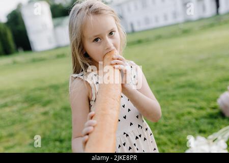 Une petite fille tient un gros pain. Drôle d'enfant heureux mord et mange du pain sain, à l'extérieur. Enfant affamé. Banque D'Images