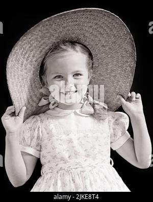 1940S JOLIE PETITE FILLE SOURIANTE AVEC DES TRESSES ET DES NOEUDS PORTANT UNE ROBE À IMPRIMÉ FLEURI TENANT SUR UN GROS CHAPEAU DE PAILLE ET REGARDANT À LA CAMÉRA - J9996 HAR001 HARS COMMUNICATION HEUREUX JOIE STYLE DE VIE FEMMES FLORALE STUDIO PRISE DE VUE SAIN MAISON VIE COPIE ESPACE DEMI-LONGUEUR EXPRESSIONS DE CONFIANCE B&W ÉTÉ JOLI SOLEIL BONHEUR JOYEUX ET EXCITANTE FIERTÉ SOURIRES ARCEAUX JOYEUX STYLÉS BRAÏDES CHARMANTS JEUNES NOIRS ET RACE BLANCHE HAR001 ANCIENNE Banque D'Images