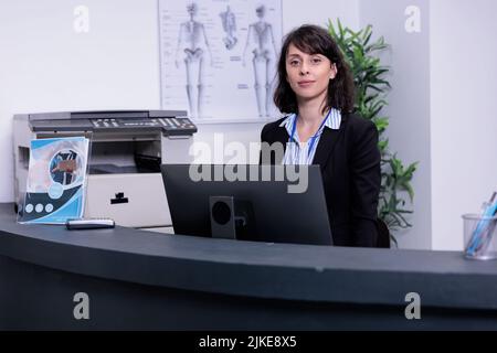 Portrait d'une réceptionniste d'hôpital souriante debout à la réception et attendant des rendez-vous à l'hôpital privé. Un professionnel de la santé accueille les patients dans le hall de la clinique privée. Banque D'Images
