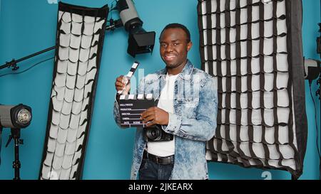 Photographe masculin tenant une ardoise de film d'action pour couper des scènes, posant dans les coulisses du studio. Personne avec un appareil photo reflex numérique disposant d'un équipement de photographie et utilisant un film clapper, réalisateur. Banque D'Images