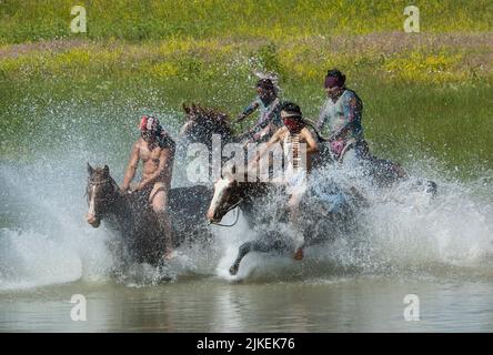 Les braves indiennes américaines font la course à la guerre à cheval en traversant la rivière Little Bighorn pendant la reconstitution annuelle du dernier stand de Custer, Montana Banque D'Images