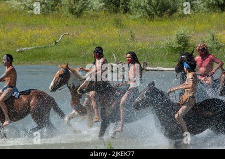 Les braves indiennes américaines font la course à la guerre à cheval en traversant la rivière Little Bighorn pendant la reconstitution annuelle du dernier stand de Custer, Montana Banque D'Images