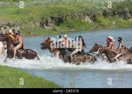 Les braves indiennes américaines font la course à la guerre à cheval en traversant la rivière Little Bighorn pendant la reconstitution annuelle du dernier stand de Custer, Montana Banque D'Images