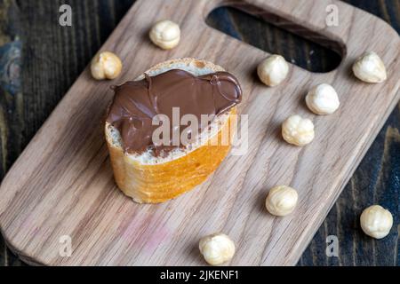 tartiner le beurre de chocolat sur une baguette, le beurre de chocolat doux sur une baguette pendant la préparation d'un simple dessert à la maison Banque D'Images