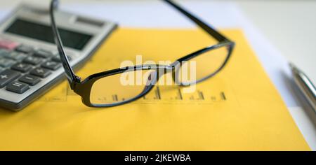 Lunettes, calculatrice et stylo en haut du rapport avec graphiques. Comptabilité financière et tendances du marché. Banque D'Images