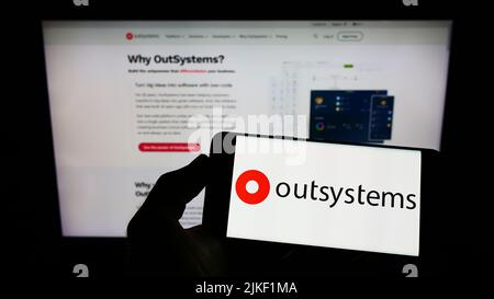 Personne tenant un smartphone avec le logo de la société de logiciel à code faible OutSystems à l'écran devant le site Web. Mise au point sur l'affichage du téléphone. Banque D'Images