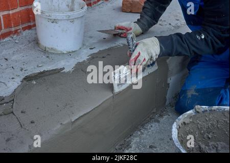 un travailleur utilise une spatule pour distribuer le mélange de ciment le long de la rampe Banque D'Images