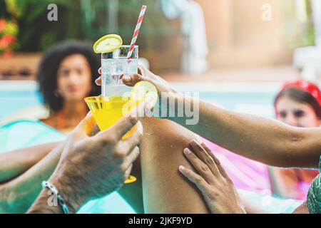 Photo rognée des mains de toasting avec des cocktails de fantaisie et des boissons alcoolisées, martini, mojito, margarita natation dans la piscine - les gens de bonheur dans le Banque D'Images