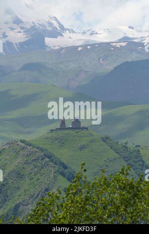 L'église de la Trinité de Gergety construite sur une haute colline couverte de verdure et d'arbres contre les montagnes dans la brume Banque D'Images