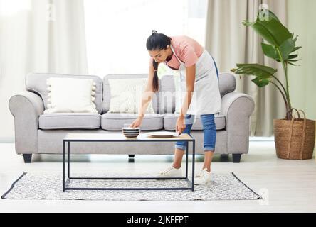 Nettoyage du désordre de la dernière nuit, séance d'observation de la frénésie. Une jeune femme qui enlève de la vaisselle sale d'une table de café dans le salon à la maison. Banque D'Images