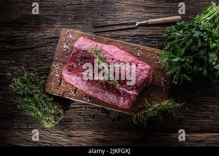 Steak de côtes de bœuf cru entier sur une planche de bois avec des herbes - dessus de la vue. Banque D'Images