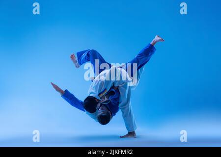 Portrait dynamique d'athlètes professionnels judo s'entraîner isolé sur fond bleu studio dans la lumière du néon Banque D'Images