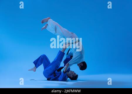 Portrait dynamique de l'entraînement professionnel des entraîneurs de judo avec un athlète isolé sur fond bleu de studio à la lumière du néon Banque D'Images