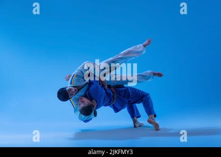 Portrait dynamique des athlètes professionnels de combat de combat de combat isolé sur fond bleu studio dans la lumière néon Banque D'Images