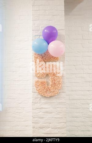 Le numéro rose 5 et les ballons sont suspendus sur un mur de briques blanches. Le décor de la chambre des enfants pour l'anniversaire de l'enfant Banque D'Images