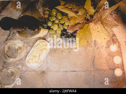 Vue de dessus du fromage, des verres à vin blanc, du raisin et des feuilles d'automne avec une bouteille de vin. Plat de préparation de vin et image d'arrière-plan. Banque D'Images