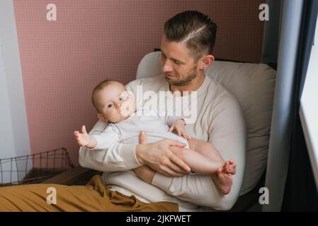 Portrait d'un père caucasien attentionné tenant un bébé mignon dans les bras, assis dans une chaise confortable à la maison Banque D'Images