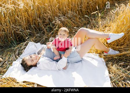 Une mère heureuse et son petit fils sont allongés sur une couverture lors d'un pique-nique. Des moments drôles en famille dans le champ en plein air Banque D'Images