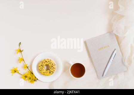 Cadre de bureau à domicile avec bloc-notes, tasse de thé, beignet, stylo. Position plate, vue de dessus. Copier l'espace Banque D'Images