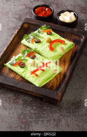 Monstre burrito drôle pour enfants avec sauces sur un plateau en bois sur la table. nourriture d'halloween. Verticale Banque D'Images