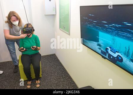 Koblenz, Allemagne. 02nd août 2022. Katrin Eder (v, Verts), ministre de la protection du climat, de l'Environnement, de l'Energie et de la mobilité de Rhénanie-Palatinat, teste un jeu de réalité virtuelle dans le Mosellum, le monde de l'aventure au barrage de Moselle à Koblenz, qui vise à attirer l'attention sur le problème de la pollution microplastique des eaux et de leurs habitants. Les visiteurs peuvent l'utiliser pour s'immerger dans le monde sous-marin de la Moselle sous la devise « les déchets plastiques mettent nos eaux en danger ». Crédit : Thomas Frey/dpa/Alay Live News Banque D'Images