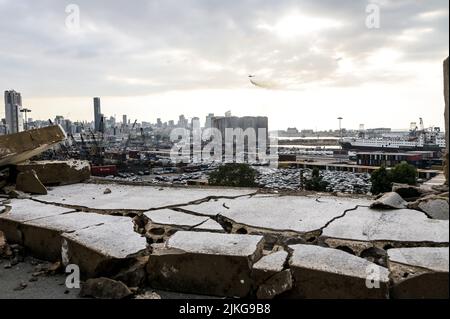 Beyrouth, Liban, le 31 juillet 2022. Des hélicoptères d'eau au travail après que deux silos du bloc nord des silos à céréales du port de Beyrouth se sont effondrés, après plus de deux semaines de feux de grains fermentés à l'intérieur de la structure fortement endommagée lors de l'explosion du port de Beyrouth le 4 août 2020, Vu ici à travers les décombres d'un bâtiment endommagé par une explosion qui est resté intact au cours des deux années qui ont suivi l'explosion. Banque D'Images