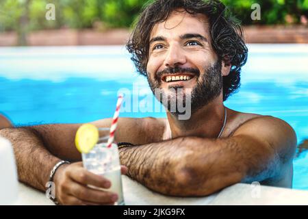 Portrait d'un homme poilu se relaxant en buvant un cocktail rafraîchissant et en discutant avec des amis tout en prenant un bain dans la piscine - concept de vacances d'été Banque D'Images