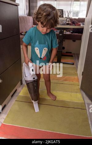 Mignon et diligent bébé nettoie la caravane avec un aspirateur. Banque D'Images