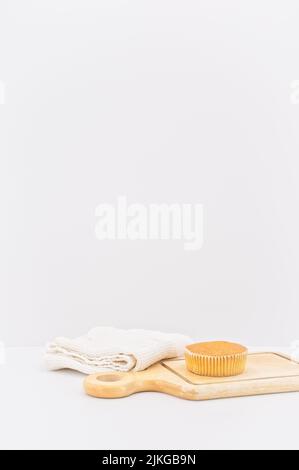 gâteau de carottes bio dans une tasse en papier avec farine d'épeautre, serviette de cuisine et planche à découper en bois sur une table blanche Banque D'Images