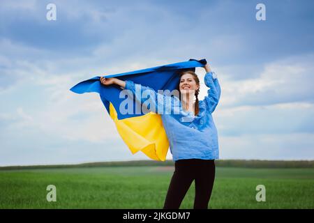 Une femme ukrainienne gratuite heureuse avec drapeau national sur fond de ciel spectaculaire. Portrait de dame en bleu broderie vyshyvanka chemise. Ukraine, indépendance Banque D'Images