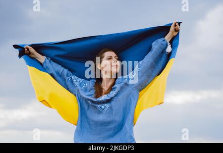 Une femme ukrainienne gratuite heureuse avec drapeau national sur fond de ciel spectaculaire. Portrait de dame en bleu broderie vyshyvanka chemise. Ukraine, indépendance Banque D'Images