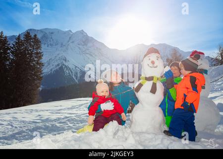 Famille avec mère, fille et deux garçons construire bonhomme de neige dans les montagnes Banque D'Images