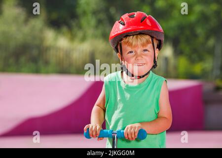 Gros portrait petit garçon sur la promenade en scooter et grand sourire Banque D'Images