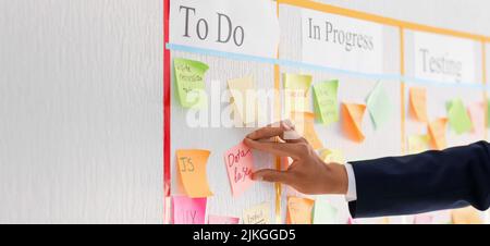 Homme d'affaires attachant un pense-bête au tableau de travail de la mêlée dans le bureau, en gros plan Banque D'Images